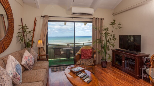 A living room with a sofa, a coffee table with remotes, a television, and a view of the ocean. - Spacious 1 Bedrm Unit. Stunning Ocean View, in South Kihei, Maui.  (Kihei)