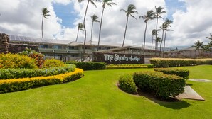 A hotel entrance with a sign reading "The Shores of Maui," surrounded by well-manicured lawns and palm trees. - Spacious 1 Bedrm Unit. Stunning Ocean View, in South Kihei, Maui.  (Kihei)