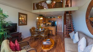 A spacious living area with a high ceiling fan, wooden flooring, a dining set, and a kitchen in the background. - Spacious 1 Bedrm Unit. Stunning Ocean View, in South Kihei, Maui.  (Kihei)
