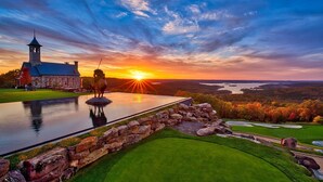 A golf course with a statue, a stone wall, and a building with a tower.