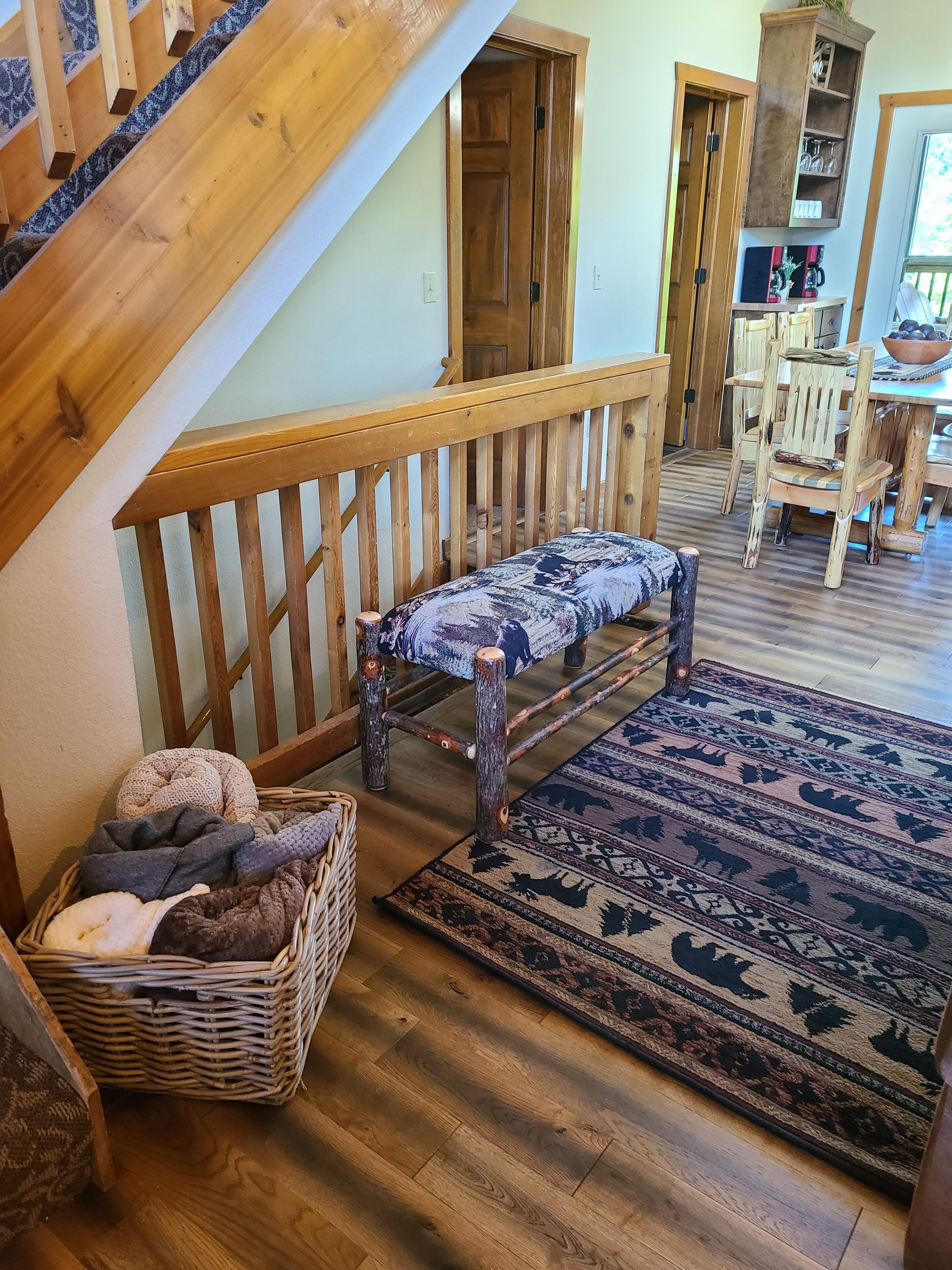 Un escalier en bois avec un banc, un panier en osier rempli de couvertures et un tapis à motifs sur un plancher en bois.