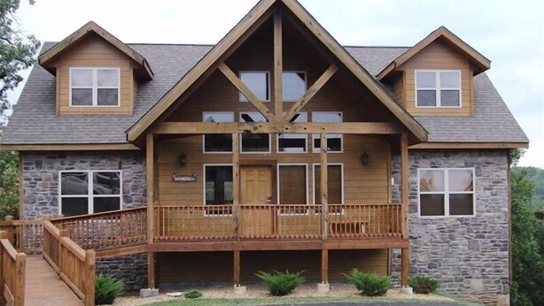 A two-story log cabin with a stone exterior, a wooden deck, and a stone staircase leading to the entrance.
