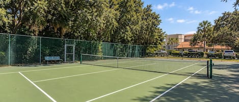Una cancha de tenis con una red, rodeada de árboles y una valla.