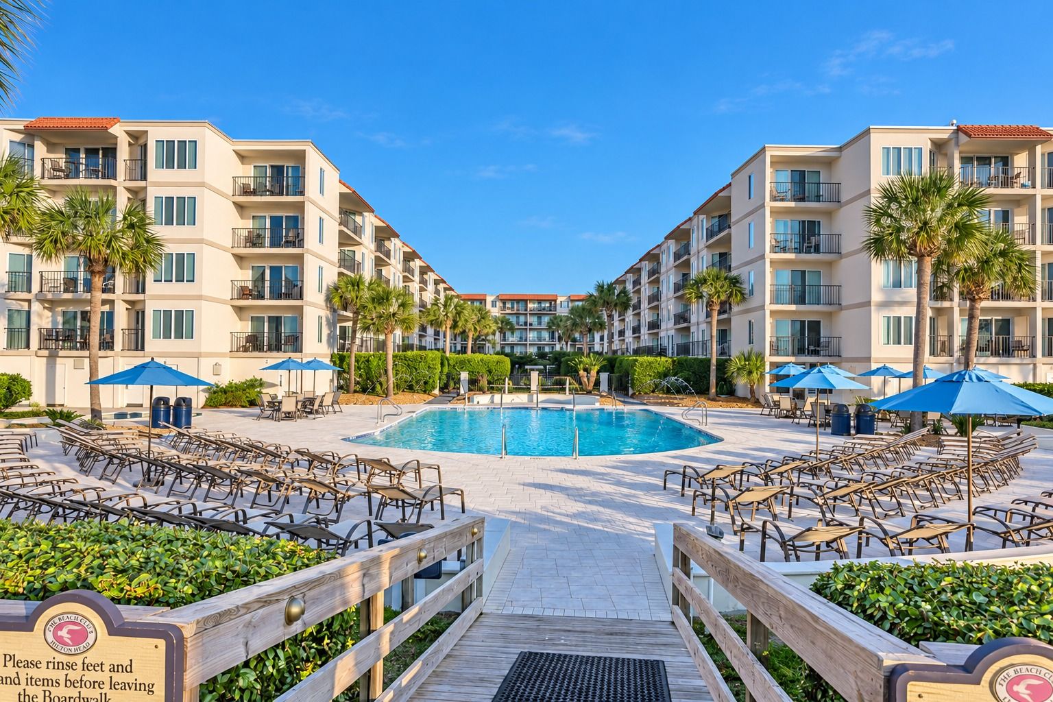 A hotel pool area with a wooden deck leading to the pool, surrounded by lounge chairs and umbrellas.