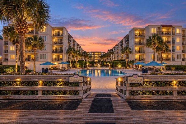A resort with a central pool, multiple balconies, and a wooden deck leading to the pool.