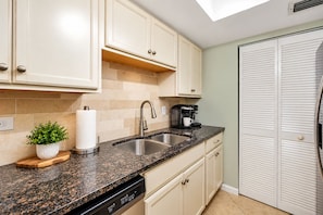 A kitchen with a granite countertop, stainless steel sink, and a coffee maker.