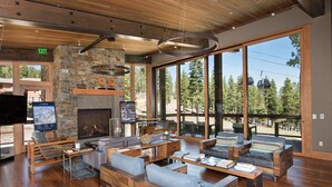 Amplia sala de estar con chimenea de piedra, mobiliario de madera y grandes ventanales con vistas al exterior.