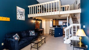A cozy living room with a dark blue sofa, a glass coffee table, and a kitchen area in the background. - ✨ Mountain Village Studio Loft ⎮Fireplace + WIFI + Hot Tubs (Steamboat Springs)