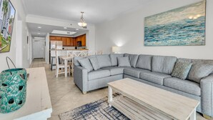 A modern living room with a grey sectional sofa, a wooden coffee table, and a kitchen in the background.