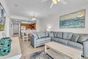 Ein modernes Wohnzimmer mit einem grauen Ecksofa, einem Holztisch und einer Küche im Hintergrund.