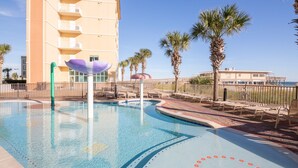 A swimming pool with a curved design, surrounded by palm trees and a building with balconies.
