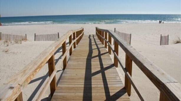 A wooden boardwalk leading to a beach with a clear view of the ocean.