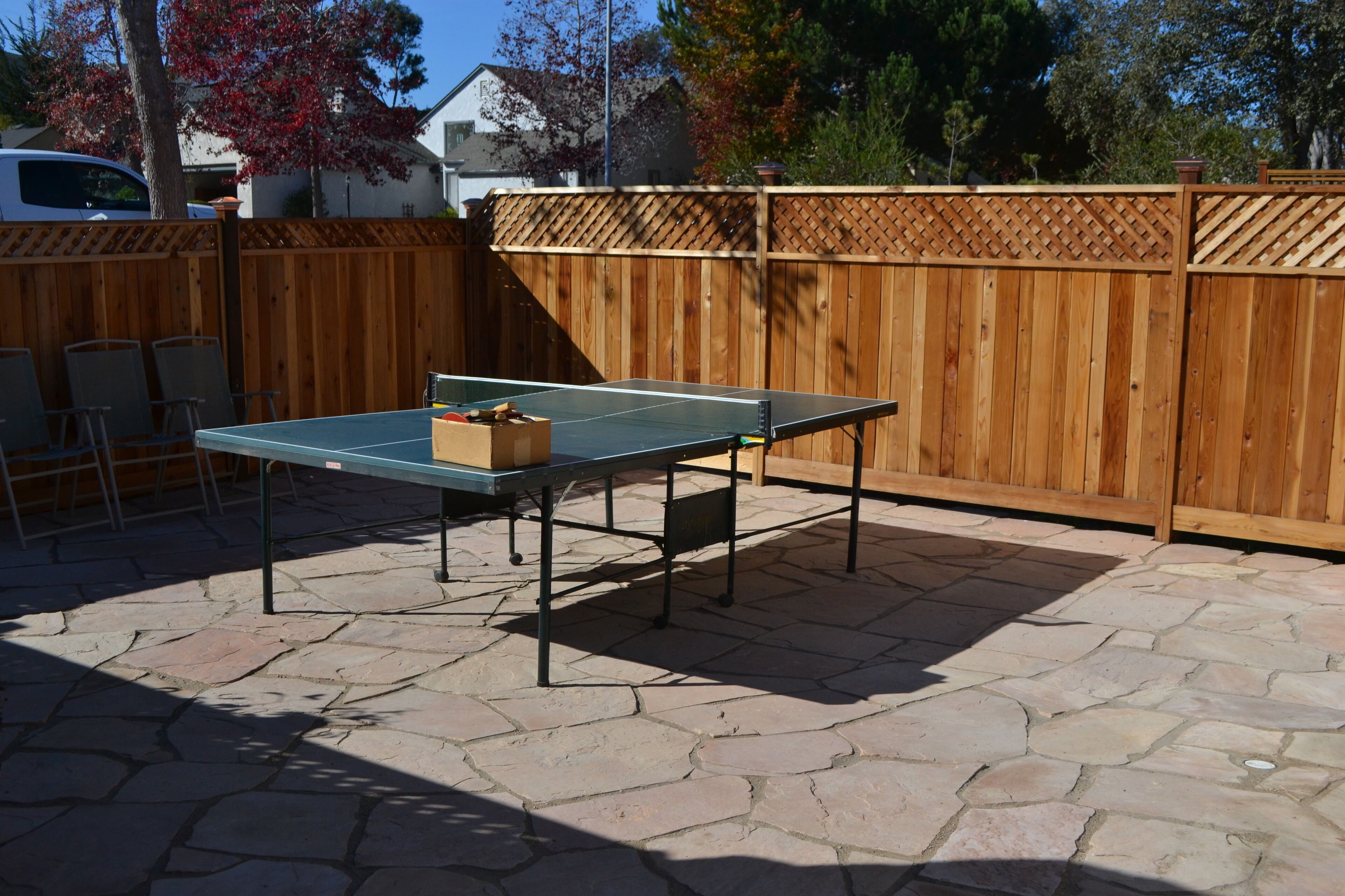 A ping pong table in a backyard with a wooden fence and stone patio.