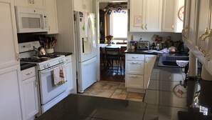 Una cocina con armarios blancos, microondas, estufa, refrigerador y piso de baldosas.