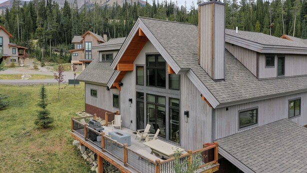 A modern multi-story house with a deck, large windows, and a mountainous backdrop. - 5 Claim Jumper | Ski-in/Out Chalet, Hot Tub (Big Sky)