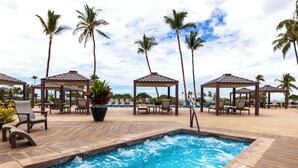A pool area with lounge chairs and gazebos, surrounded by palm trees.