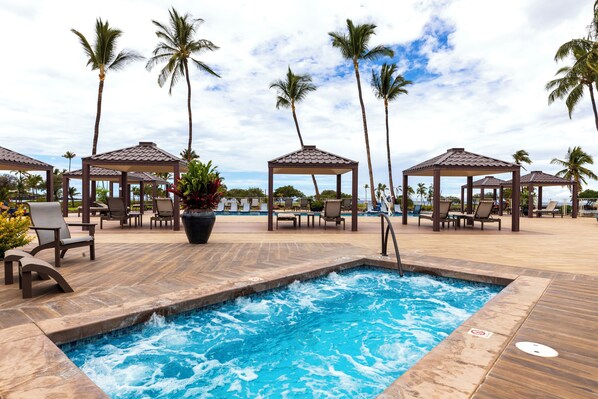 A pool area with lounge chairs and gazebos, surrounded by palm trees.
