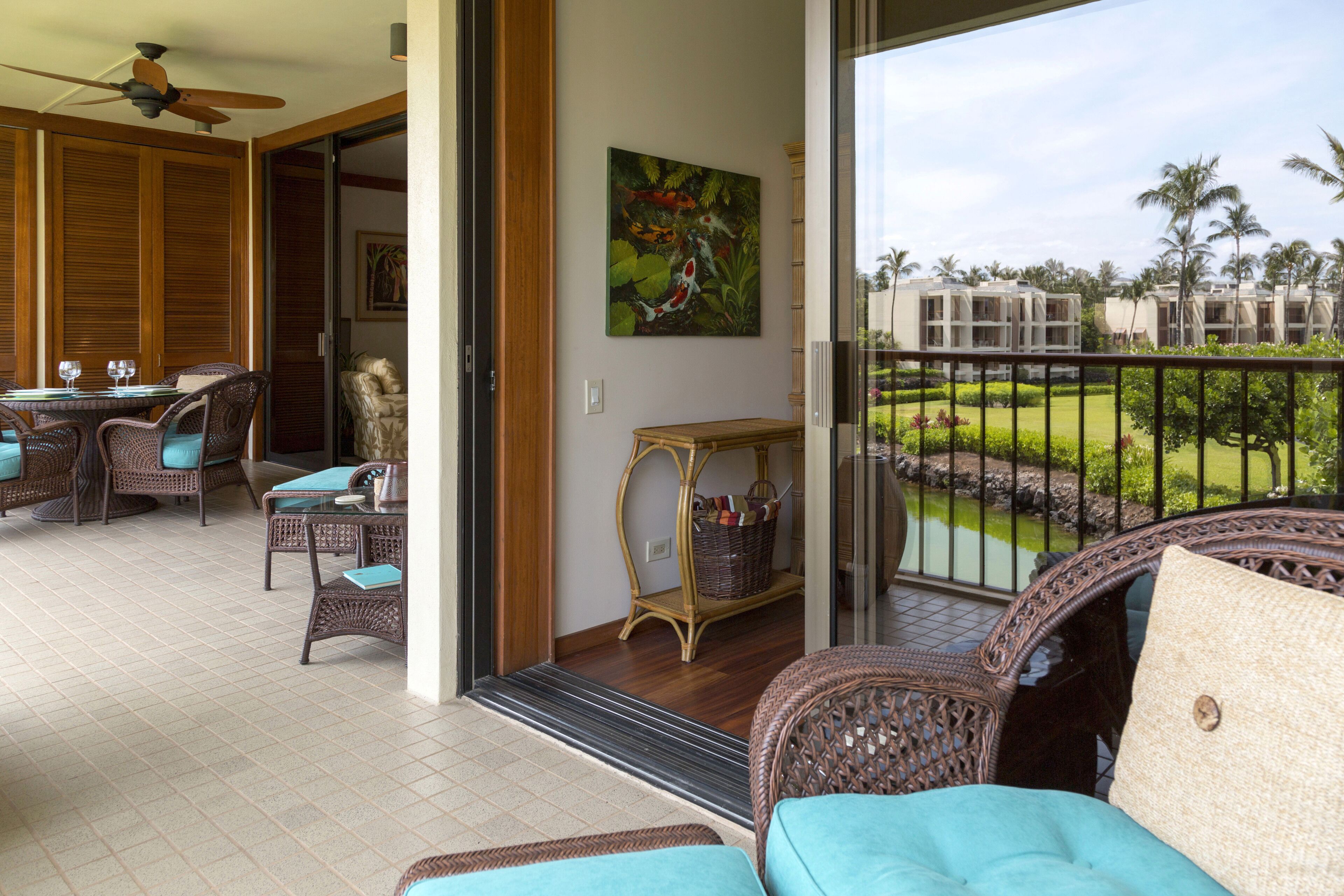 Un balcone con mobili in vimini, un'area pranzo e vista su un resort con palme.