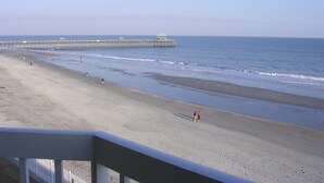 A beach with a pier extending into the ocean, a clear sky, and a few people walking along the shore.