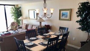 A dining area with a table set for six, surrounded by chairs, a chandelier, and a sofa in the background.