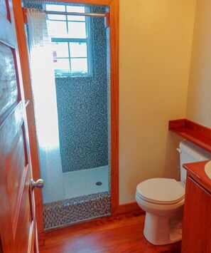 Un baño con zona de ducha, inodoro y tocador de madera.