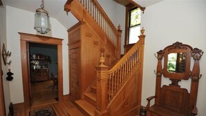A wooden staircase with a handrail and a chandelier, leading to a room with a large mirror and a door.