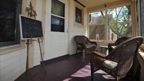 A cozy room with a chalkboard sign reading "WELCOME TO THE BIRDSHORE," wicker chairs, and large windows offering a view of the outside.