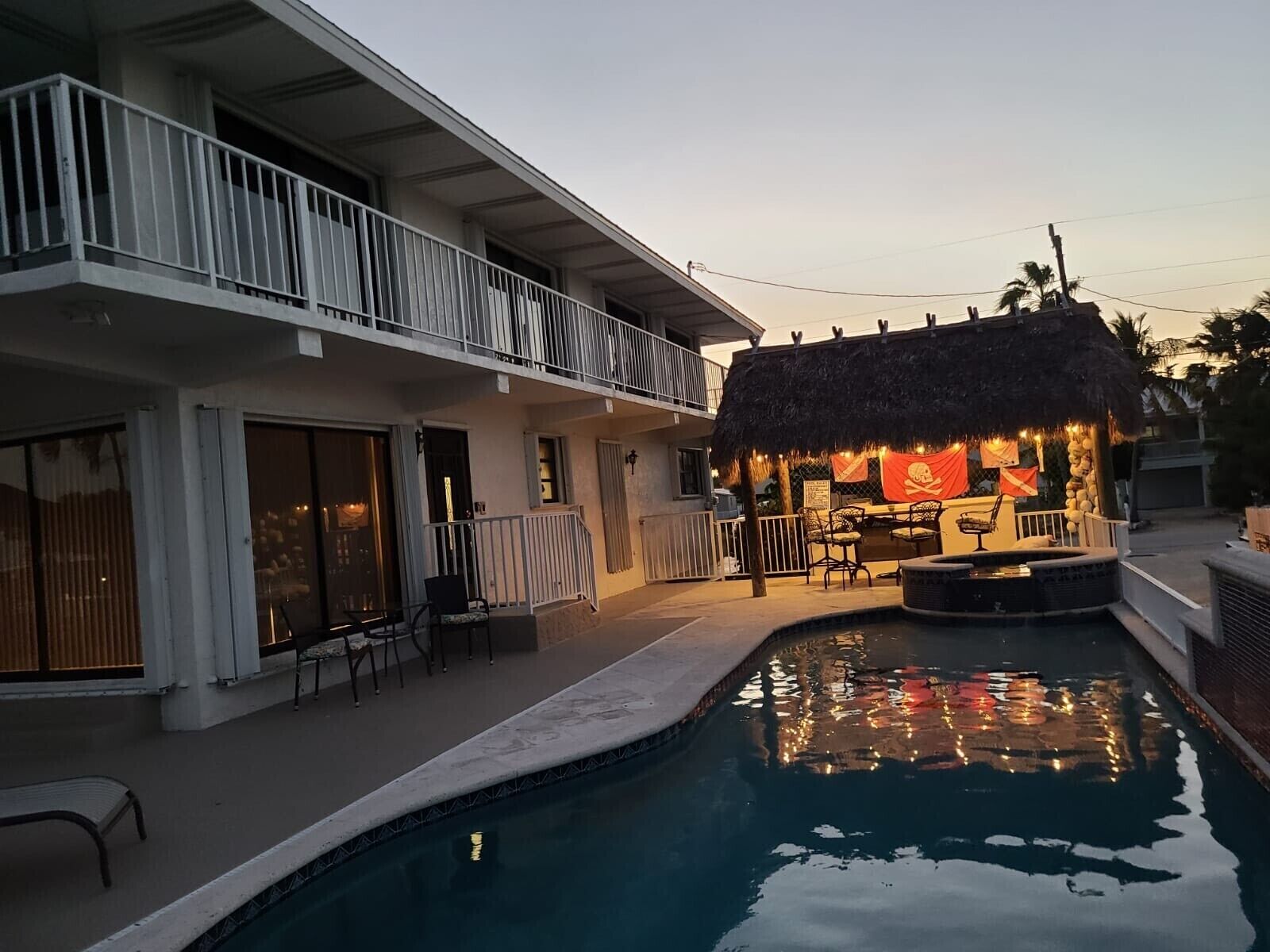A poolside area with a bar and seating, a thatched-roof structure, and a balcony.