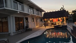 Ein Poolbereich mit Bar und Sitzgelegenheiten, einer Struktur mit Reetdach und einem Balkon.
