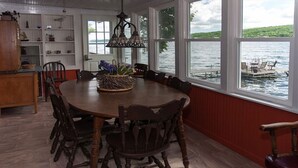 Un espace repas avec une grande table en bois entourée de chaises, un lustre et une vue sur un lac.