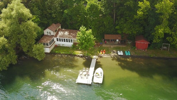 Une propriété située au bord de la rivière, avec un quai, une maison blanche et un abri de jardin rouge.