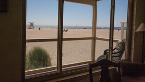 Een kamer met grote ramen met uitzicht op een strand. Er staat een stoel en een tafel in de kamer.