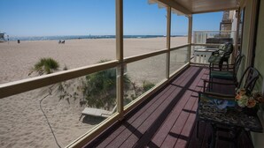 Uitzicht op het strand vanaf een overdekt terras met houten vloer en metalen hekwerk.