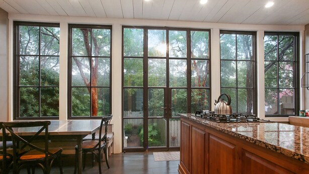 A kitchen with large windows, a dining area with chairs, and a wooden countertop.