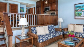 A spacious living area with a sofa set, a coffee table, and a dining area with wooden cabinets and a microwave.