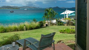 A patio with a table and chair overlooking a turquoise sea with boats, a white gazebo, and lush greenery.