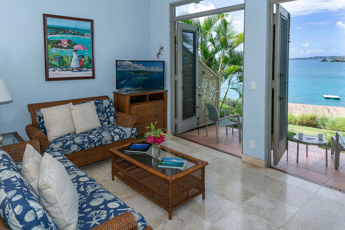 A living room with a sofa, coffee table, TV, and a view of the sea through an open door.