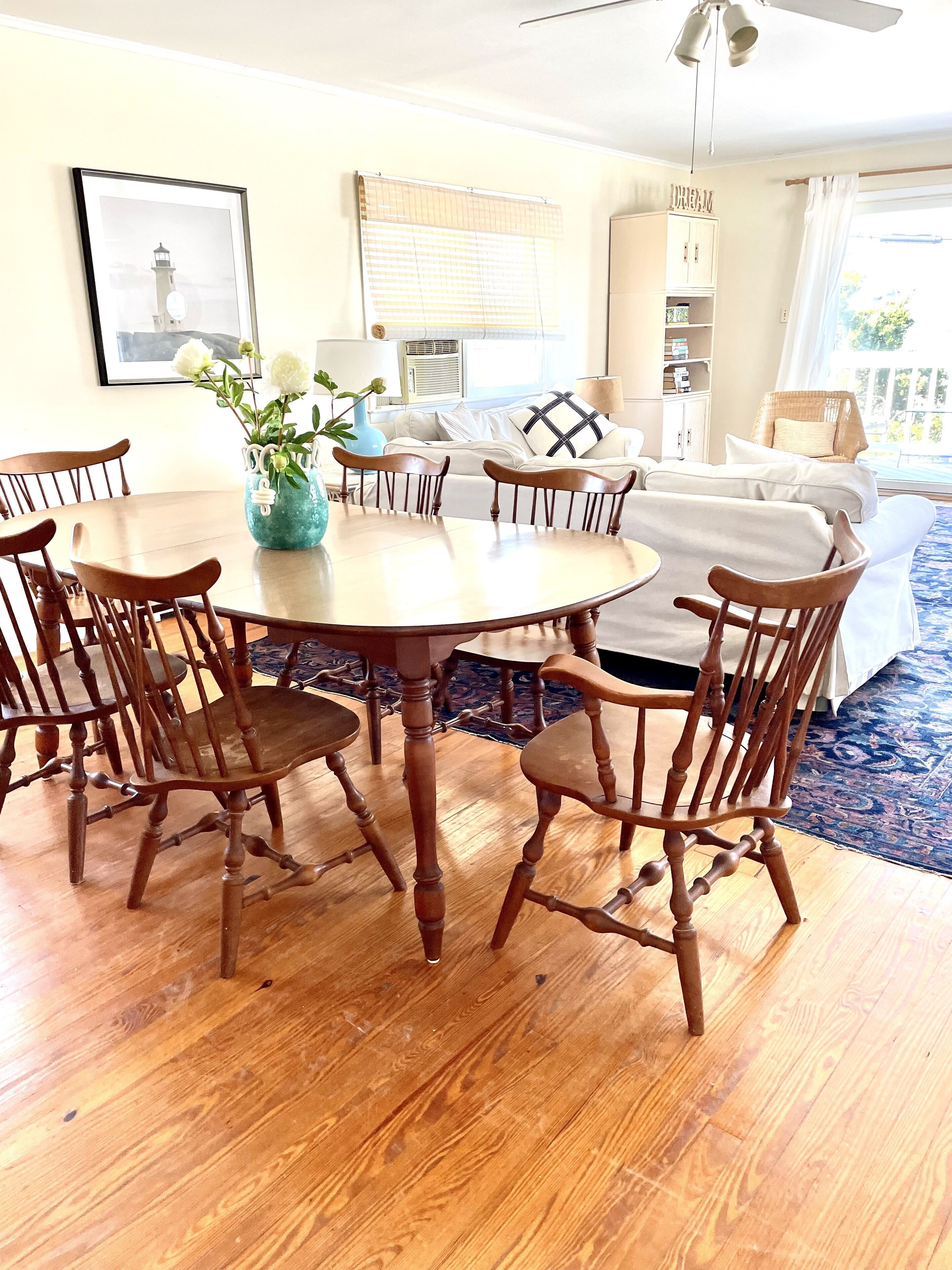 A dining area with a round wooden table and six chairs, a vase with flowers, and a ceiling fan.