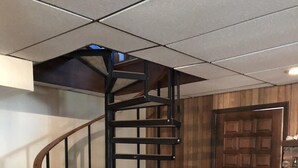Un escalier en colimaçon avec une rampe en bois et une structure en métal noir, menant à l’étage supérieur.