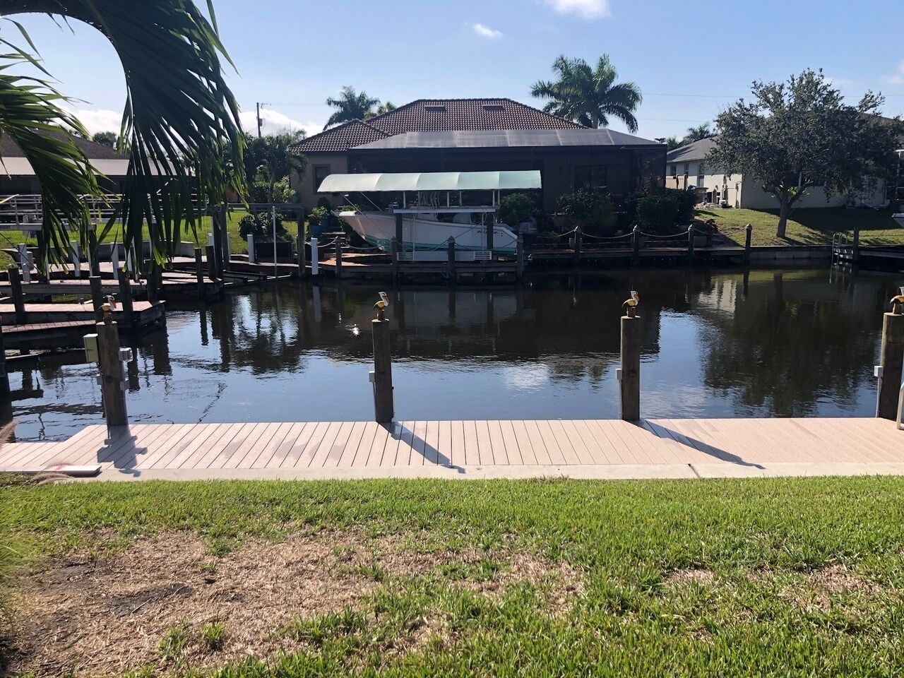 A calm water body with a dock, a covered boat house, and a grassy area in the foreground.