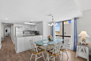 Une cuisine moderne avec des meubles blancs, un îlot central en verre et un coin repas comprenant une table et des chaises en verre.