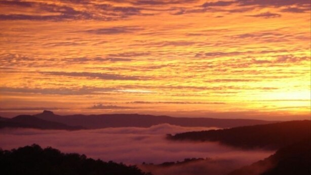 A sunset over a mountainous landscape with clouds below.
