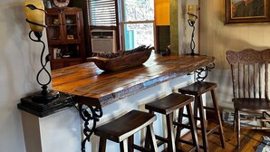 A rustic kitchen with a wooden island, bar stools, a large mirror, and a painting on the wall.