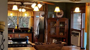 A rustic kitchen with wooden cabinets, a large wooden bowl on the counter, and pendant lights.