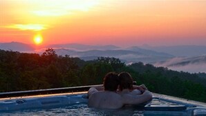 A couple in a hot tub overlooking a mountainous landscape at sunset.