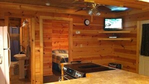 A kitchen with a wooden interior, a ceiling fan, a clock, and a television on a shelf.