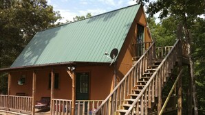 A cabin with a wooden deck, a staircase, and a green roof.