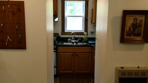A kitchen with wooden cabinets, a window above the sink, and a framed picture on the wall. - Solar powered cottage at lake, with dock, on private 300 acre timber preserve (Clarksville)