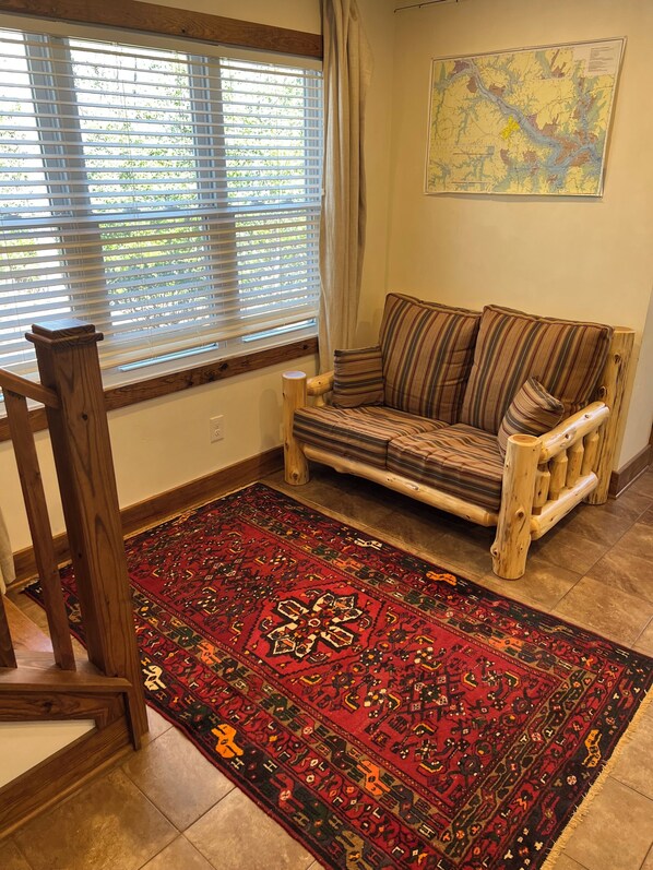 A room with a wooden sofa, a patterned rug, a wooden chair, and a map on the wall.