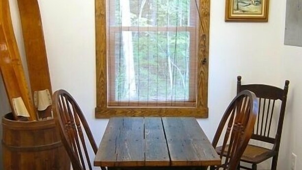 A rustic wooden table with two chairs, a wooden barrel, and a window with a view of trees. - Solar powered cottage at lake, with dock, on private 300 acre timber preserve (Clarksville)